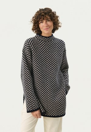 Navy and cream herringbone-patterned knit sweater with a high collar, loose fit, and side slits, made from a soft texture.