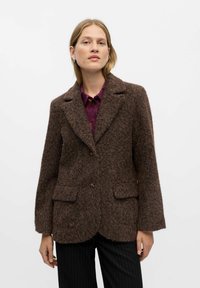 Brun tekstureret blazer med spidse rever, enkelt knaplukning og to forlommer, parret med en lilla skjorte og stribede bukser.