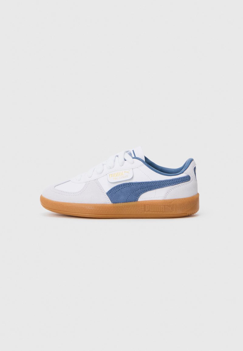Sneaker bianca con accenti in suede blu, suola in gomma testurizzata e design con lacci. Presenta un'etichetta con il logo PUMA sul lato.