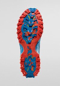 Podešev běžecké obuvi do terénu v modré a červené barvě. Disponuje texturovanou gumou s agresivními výstupky pro trakci a barevnými akcenty.