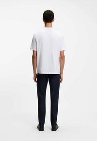 Biała bawełniana koszulka z klasycznym okrągłym dekoltem, krótkimi rękawami i prostym krojem, zestawiona z ciemnoniebieskimi dżinsowymi spodniami i czarnymi butami.