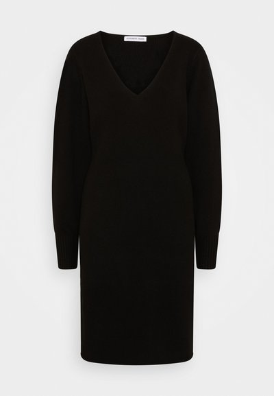 Vestido preto, de malha, com decote em V e mangas longas. A silhueta justa apresenta punhos canelados e uma bainha reta.