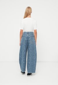 Wijde jeans in lichtblauw denim met een subtiel slangenprintpatroon. Achteraanzicht toont twee zakken en een hoog tailleontwerp.