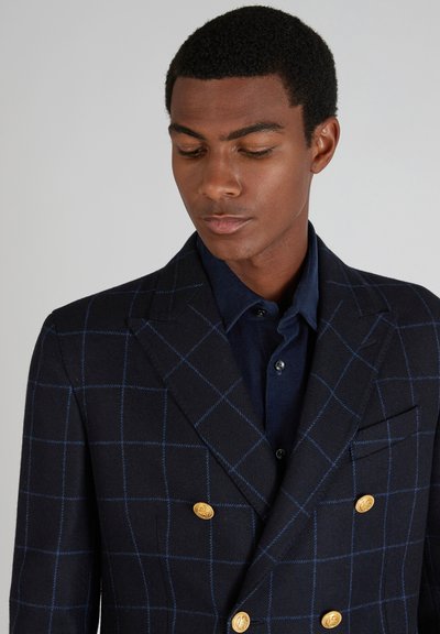 Marineblau kariertes Zweireiher-Blazer mit blauen Linien, goldenen Knöpfen und Aufschlägen, getragen über einem dunkelblauen Hemd. Strukturierten Stoff.
