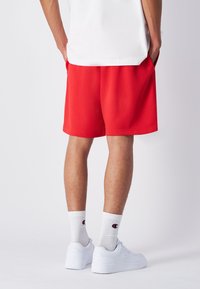 Pantalones cortos rojos de tela suave, con un ajuste holgado y bolsillos laterales, combinados con zapatillas blancas y calcetines de canalé con logo.