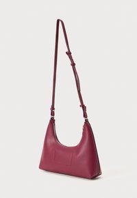Burgundi bőr válltáska ívelt formával, állítható pánttal és ezüst cipzár részletekkel. Simogatós textúra és minimalista díszítések.