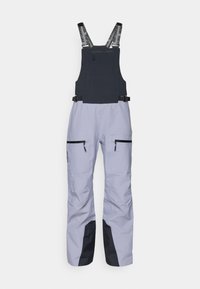 Smučarski kombinezoni svetlo sive barve z kontrastnim črnim panelom na dnu. Imajo prilagodljive naramnice in dva črna žepa z zadrgo.