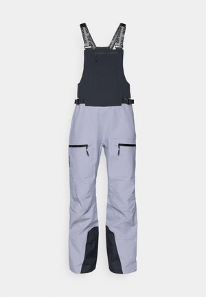 Salopettes de ski en gris clair avec un panneau noir contrastant en bas. Dotées de bretelles réglables et de deux poches zippées noires.