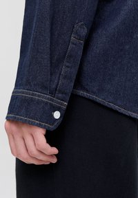 Mørkeblå denimskjorte med knapmanchetter, med hvite knapper og kontrastsøm. Glatt tekstur med et klassisk design.
