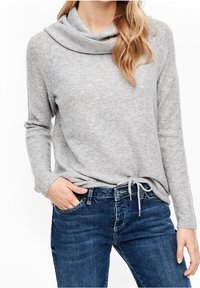 Maglione grigio con scollo a cowl in un morbido tessuto testurizzato, con maniche lunghe e un accento con cordino in vita, abbinato a jeans blu.