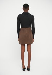 Svart figurnær langermet topp og brun suede miniskjørt. Skjørtet har rett snitt og usynlig glidelås bak. Enkel hvit bakgrunn.