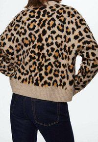 Pull à motif léopard beige avec des taches noires et marron ; ourlet côtelé ; texture douce ; porté avec un jean en denim foncé.