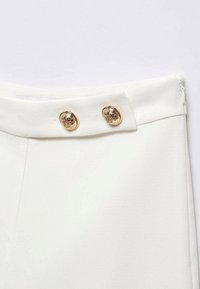 Witte broek met een gladde textuur, voorzien van twee gouden decoratieve knopen op de taille en een ritssluiting aan de zijkant.