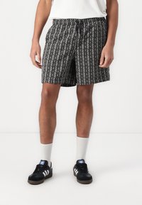 Shorts à motifs noir et blanc avec des rayures verticales, taille élastique et détails de cordon de serrage. Associés à des baskets noires et des chaussettes blanches.