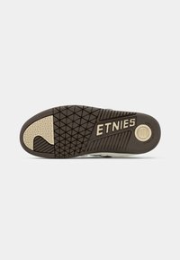 Sola do ténis Etnies em material de borracha castanha, apresentando um padrão de textura para aderência e logótipo "ETNIES" em dourado. Acentuada com um bloco de cor mais clara.