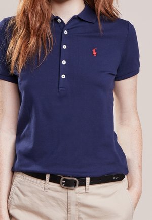 Polo bleu marine en coton texturé, avec un col côtelé, cinq boutons blancs et un logo rouge brodé sur la poitrine gauche.