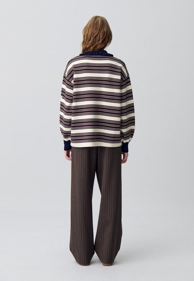 Maglione a righe in crema e bordeaux con colletto a balze blu scuro, abbinato a pantaloni a gamba larga marroni a righe, visto da dietro.