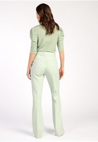 Mintgrünes, geripptes Oberteil mit Puffärmeln, kombiniert mit hoch taillierten, weit geschnittenen hellgrünen Hosen. Glattes Material mit einem maßgeschneiderten Look.
