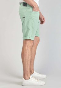 Shorts vert menthe avec ourlets retroussés, en tissu léger, dotés de poches latérales et d'un accent noir sur la poche arrière. Associés à des baskets blanches.