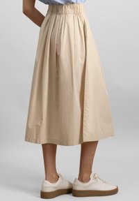 Beige pleated skirt with an elastic waistband, mid-calf length, and soft texture, paired with white sneakers and a minimalistic design.