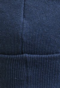 Granatowa dziana czapka z ribbowanym wykończeniem, z podwiniętym mankietem i gładką powierzchnią na całej długości. Materiał wydaje się miękki i ciepły.