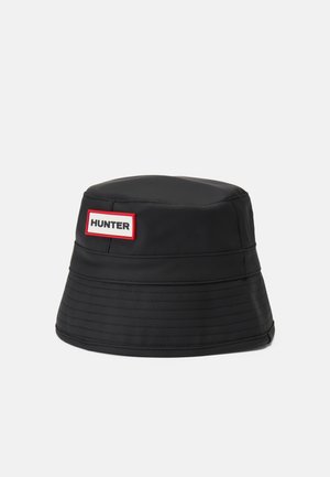 Chapeau seau noir avec une couronne arrondie et un large bord inclinant vers le bas. Présente un patch logo rectangulaire rouge et blanc sur lequel est inscrit "HUNTER".