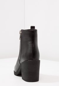 Stivaletto nero con tacco alto realizzato in pelle liscia, dotato di zip laterale, punta arrotondata e tacco a blocco testurizzato.