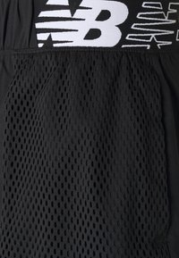 Pantalones cortos deportivos negros con textura de malla y aberturas circulares, una cinturilla sólida que presenta un logo blanco, y una tela lisa en la parte inferior.