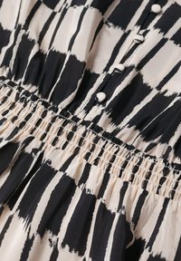 Tejido de estampado en blanco y negro con rayas verticales, que presenta una cintura fruncida y botones de tela redondos a lo largo del centro. Textura ligera.