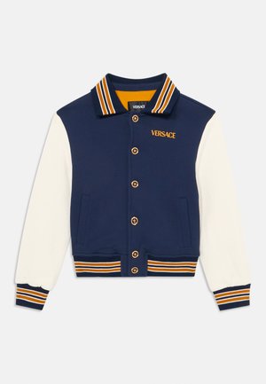Námornícky a krémový varsity kabát s pruhovaným golierom a manžetami. Obsahuje zlaté gombíky a logo "VERSACE" v oranžovej farbe. Mäkká tkanina, športový dizajn.