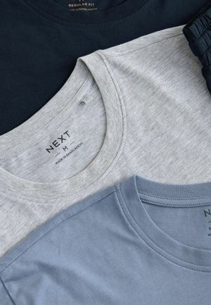 Három környakú póló egymásra rakva: egy sötétkék, egy világos szürke és egy világos kék. Mindegyik normál szabású, puha, sima anyagból készült.