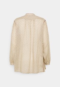 Camicia beige a maniche lunghe con un piccolo motivo a pois marroni, caratterizzata da una piega sul retro e spacchi laterali. Polsini con bottoni e colletto classico.