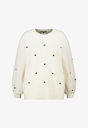Crème-kleurige sweater gemaakt van zachte stof, met een losse fit en zwarte hartpatronen verspreid over het geheel. Rond de hals en geribbelde manchetten.