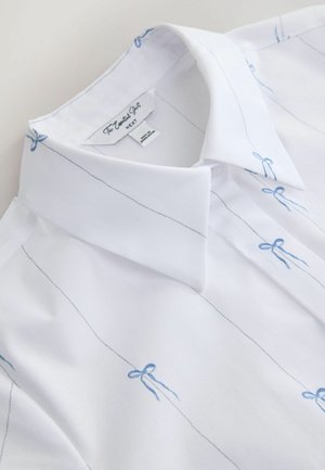 Balta krekla ar gaiši zilām vertikālām svītrām un nelielām zilām izšūtām lokām uz gludas auduma virsmas.