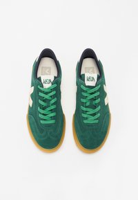 Zaļi samta sporta apavi ar zaļām auklām un gumijas zoli. Ir balti akcenti un jūras zila iekšpuse. Klasiciska sporta dizains.