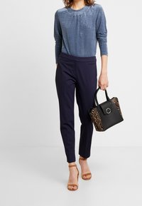 Marineblaue Hosen kombiniert mit einem strukturierten blauen Langarmoberteil. Eine Handtasche mit Tiermuster und schwarzem Grund mit einem runden Hardware-Detail.