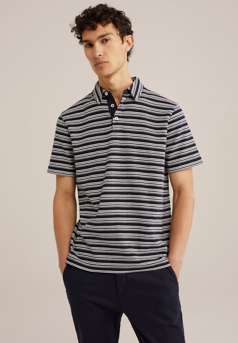 Svītrainā polo krekls tumši zilā un baltā krāsā, ar pogu aizdari, īsām piedurknēm un struktūras audumu.