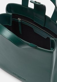 Zielona skórzana torba na ramię o gładkiej fakturze, z jedną wewnętrzną kieszenią na zamek i dwoma uchwytami. Wnętrze wyłożone jest kontrastową czernią.