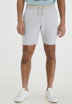 Gray cotton shorts with a beige elastic waistband and drawstring; features a frayed hem and side pockets; worn with white sneakers.