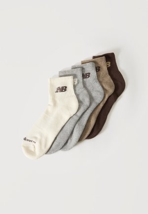 Fünf Paar New Balance Knöchelsocken in Creme, Hellgrau, Mittelgrau, Beige und Dunkelbraun, fächerförmig auf weißem Hintergrund angeordnet.
