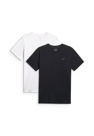 Mężczyzna stoi przodem, ubrany w czarny t-shirt, szare szorty, szare skarpetki i czarne sneakersy na jednolitym, jasnoszarym tle.