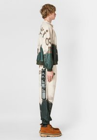 Conjunto deportivo que incluye un sudadera crema con estampados de montañas y texto, combinado con joggers estampados y botas gruesas marrones.