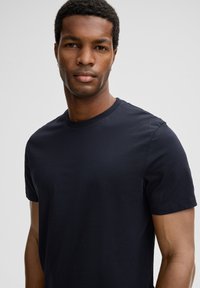 T-shirt en coton bleu marine à manches courtes et col rond, présentant une texture lisse et un design minimaliste sans accents supplémentaires.