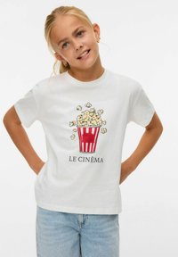 T-shirt en coton blanc avec un graphique d'un seau de popcorn rouge et blanc et le texte "LE CINÉMA" en dessous du design.