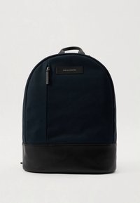 Laivastonsininen reppu pyöreällä muotoilulla, mustalla nahkapohjalla, pehmustetulla selkäosalla, yläkahvalla ja pienellä vetoketjutaskulla sivulla.