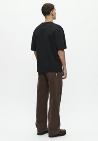 Zwarte t-shirt met korte mouwen, gecombineerd met bruin corduroy-broek met een rechte snit en zichtbare stikseldetails.