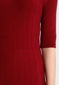 Abito a maglia rosso a coste con maniche corte, caratterizzato da righe verticali e un corpetto aderente. Texture morbida con una finitura liscia.