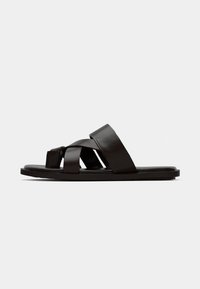 Black leather slide sandals with woven strap design, flat sole, and minimalistic silhouette. Smooth texture with no prominent embellishments.