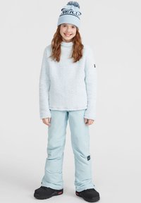 Pull bleu clair en polaire avec une finition texturée, associé à un pantalon imperméable bleu clair et des bottes de neige noires. Bonnet bleu avec pompon.