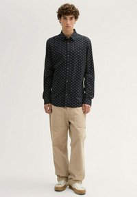 Chemise bleu marine à boutons avec de petits motifs géométriques blancs, associée à un pantalon cargo beige et des baskets beiges. Design simple et coupe décontractée.